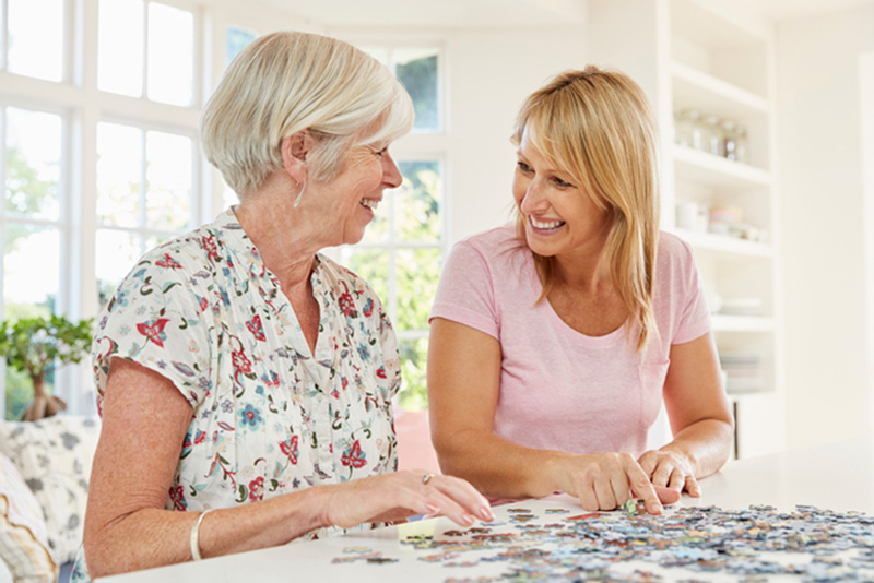 happy senior lady and caregiver putting puzzle together