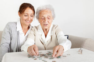 A woman smiles at her older mother while putting together a puzzle, which is one activity that can help boost self-esteem in a loved one.