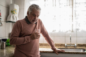 An older man stands in his kitchen with a sad look on his face, a reminder of why it is important to understand the link between depression and heart-related illnesses.