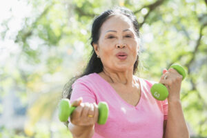 An older woman lifts hand weights, knowing exercise is a key strategy for senior stroke prevention.